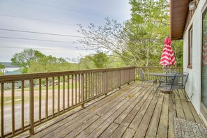 A wooden deck with a railing, a table with chairs, and a pink and white striped umbrella.