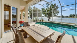 A pool area with a table and chairs, a covered patio, and a view of the lake. - Waterfront Port Charlotte Home - 5 Mi to Beach! (Port Charlotte)