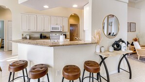 A kitchen with white cabinets, a granite countertop, and a central island with stools. - Waterfront Port Charlotte Home - 5 Mi to Beach! (Port Charlotte)