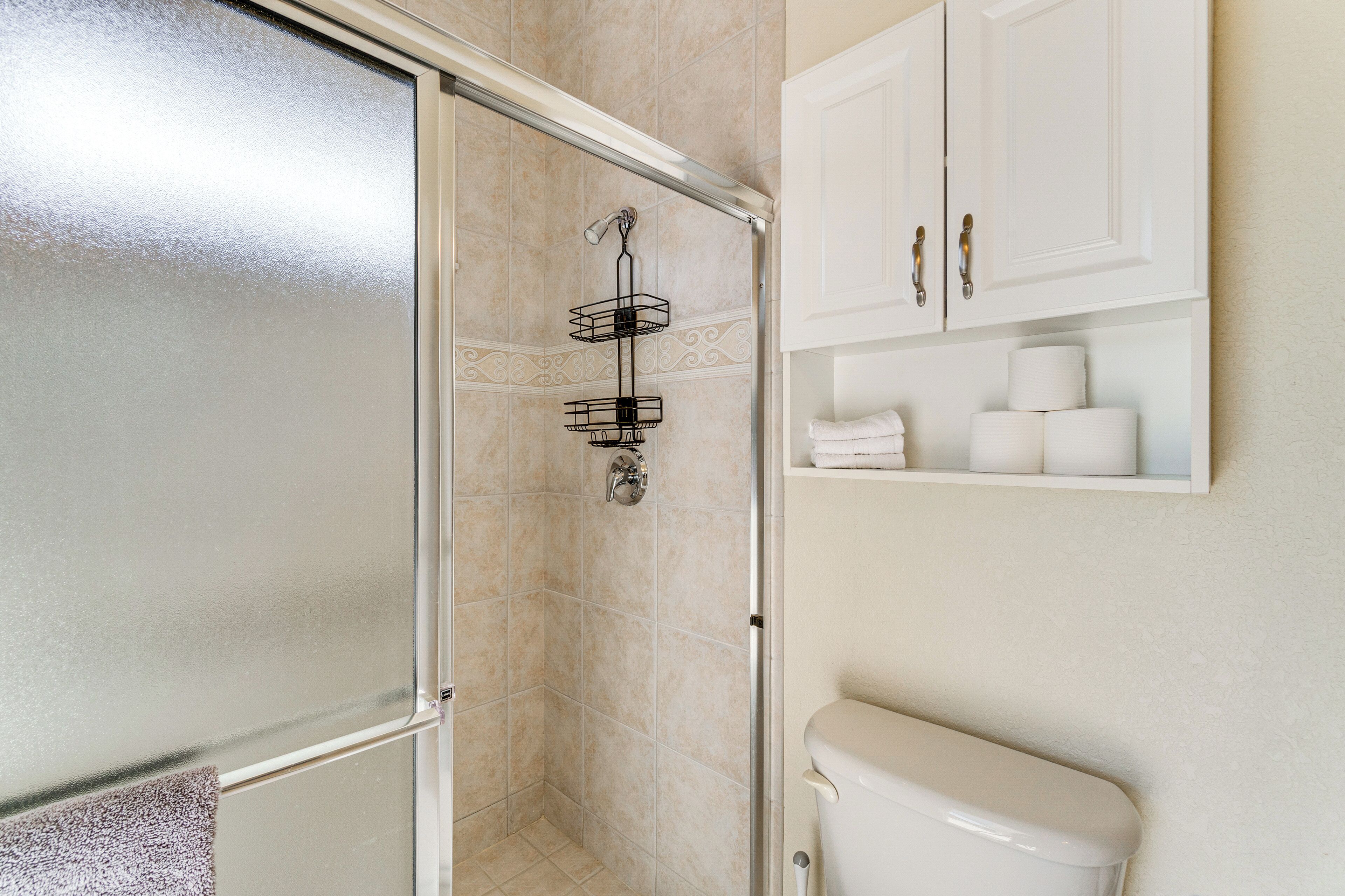 A bathroom with a glass shower enclosure, a toilet, and a shelf with toiletries.