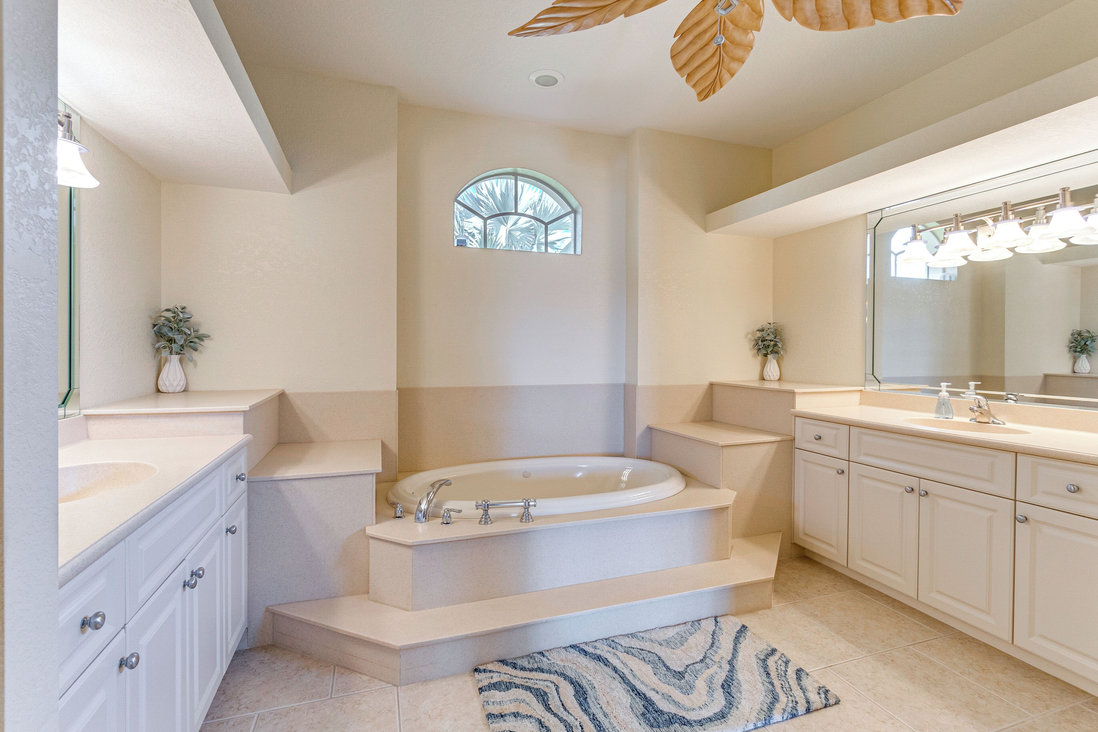 A modern bathroom with a freestanding bathtub, a large mirror, and a window with a view of palm trees.