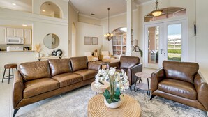 A spacious living room with a brown leather sofa, a coffee table with a floral centerpiece, and a view of the outdoors through a glass door. - Waterfront Port Charlotte Home - 5 Mi to Beach! (Port Charlotte)