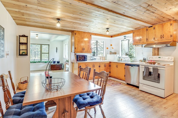 A kitchen with wooden cabinets, a dining table with blue cushioned chairs, a built-in oven, and a refrigerator. - Detroit Lake Area Cabin 1/2 Mi to Santiam River (Gates)