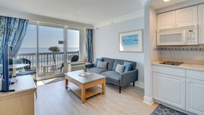 A modern living room with a grey sofa, wooden coffee table, and a view of the beach through large sliding glass doors. - Beachfront Daytona Vacation Rental w/ Balcony (Daytona Beach)