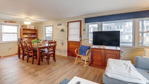 Una sala de estar con comedor, muebles de madera, televisor y ventanas amplias.