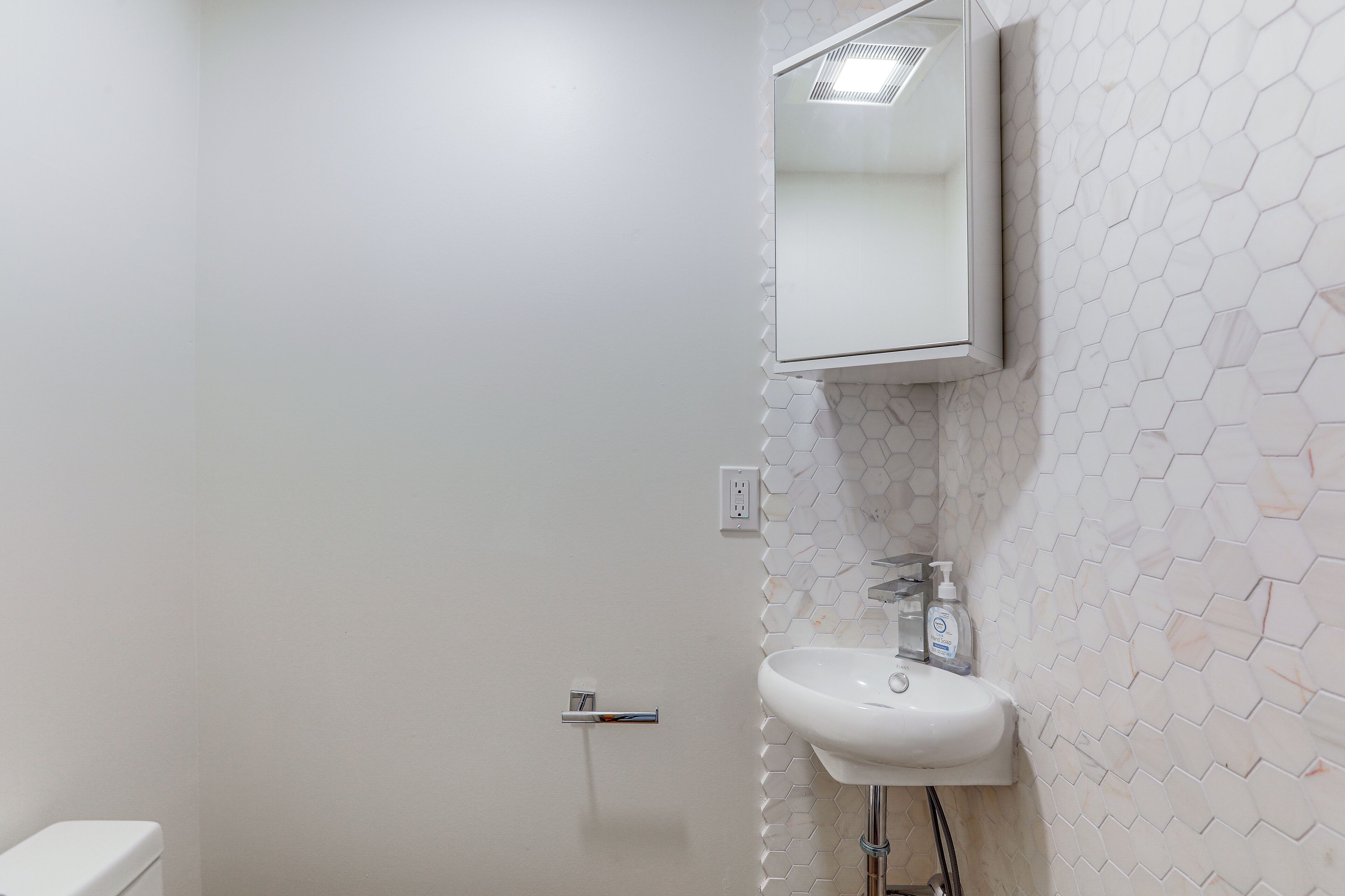 A bathroom with a white toilet, a sink with a mirror above it, and a hexagonal patterned wall.