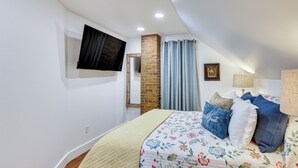 A bedroom with a bed, a flat-screen TV mounted on the wall, a brick pillar, and a window with curtains. - New Melle Apartment Near Missouri Wine Country (Wentzville)