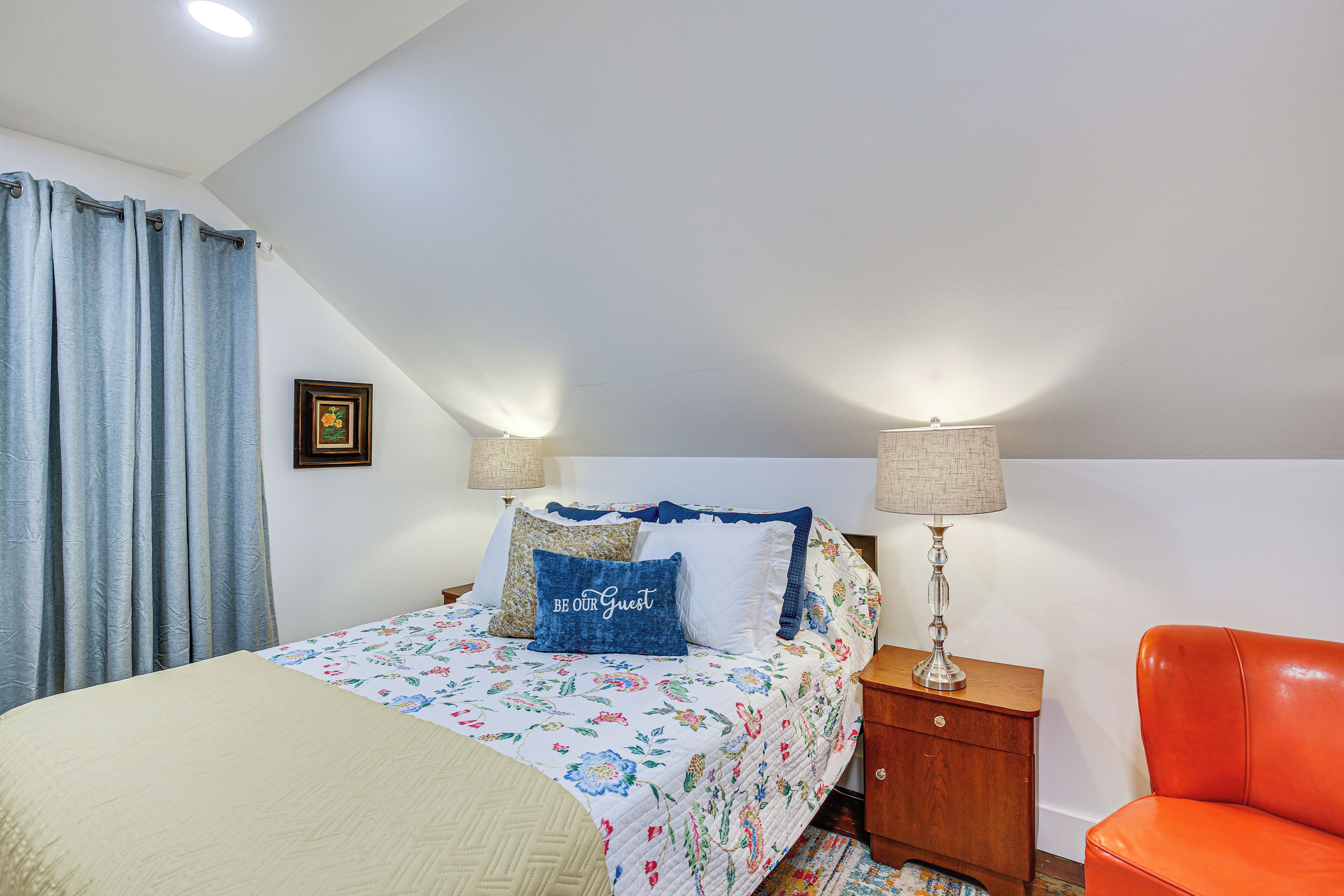 A bedroom with a bed, a nightstand, a lamp, a chair, and a window with curtains.