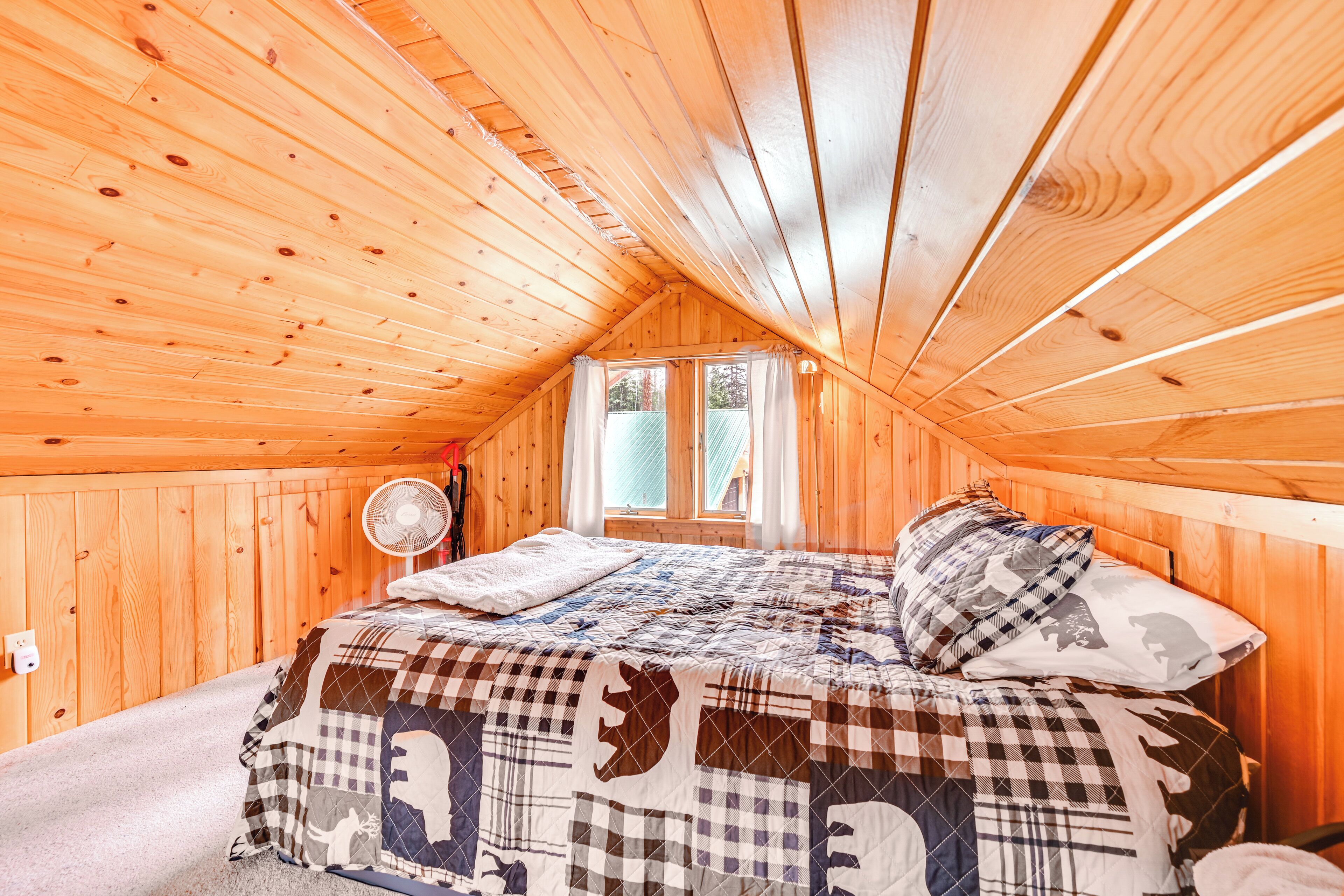 A wooden cabin bedroom with a bed, a window, and a fan.