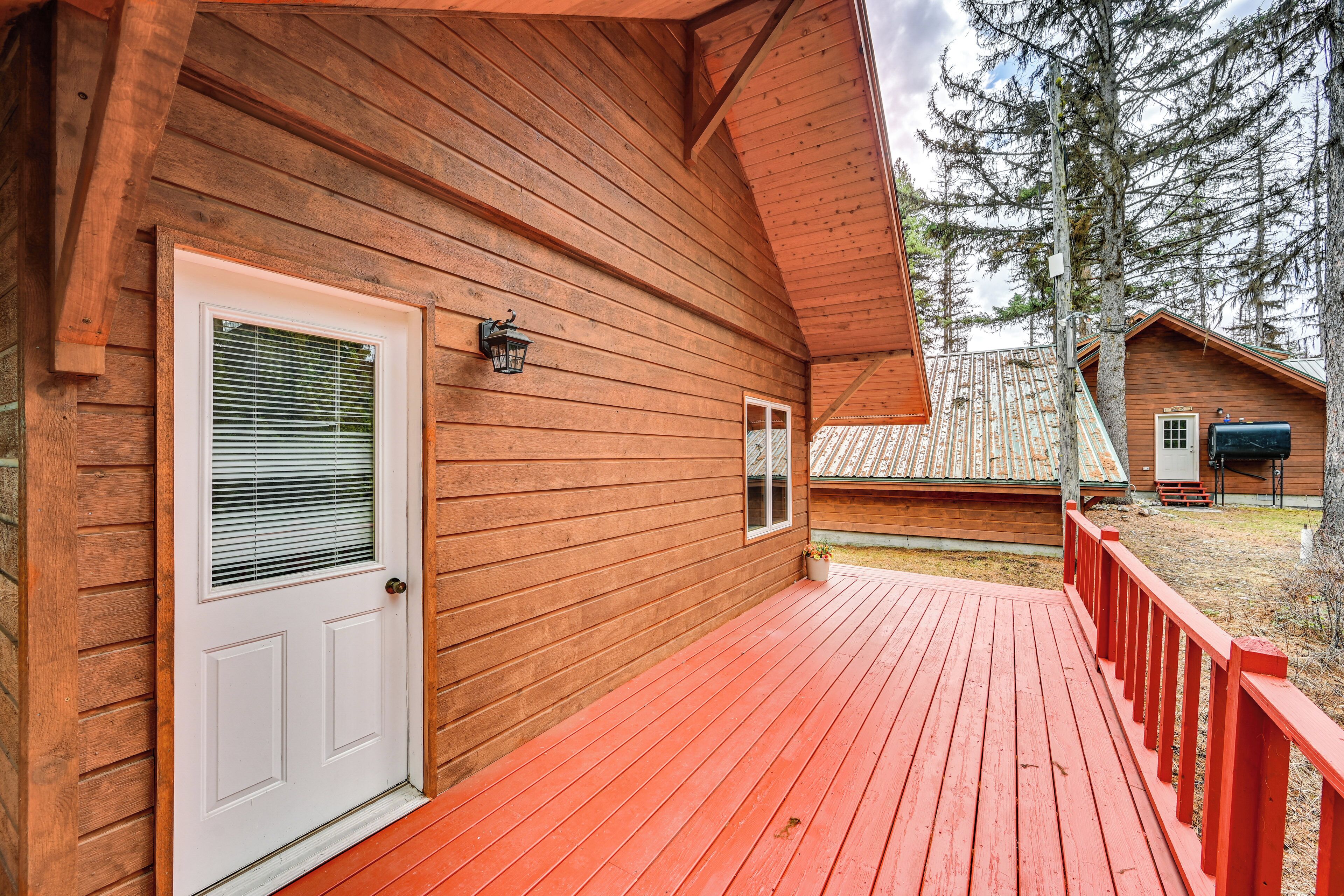 A wooden cabin with a red deck, a white door, and a small window with blinds.