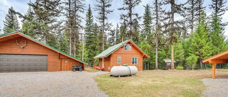 A cabin with a gravel driveway, a garage, and a small shed.