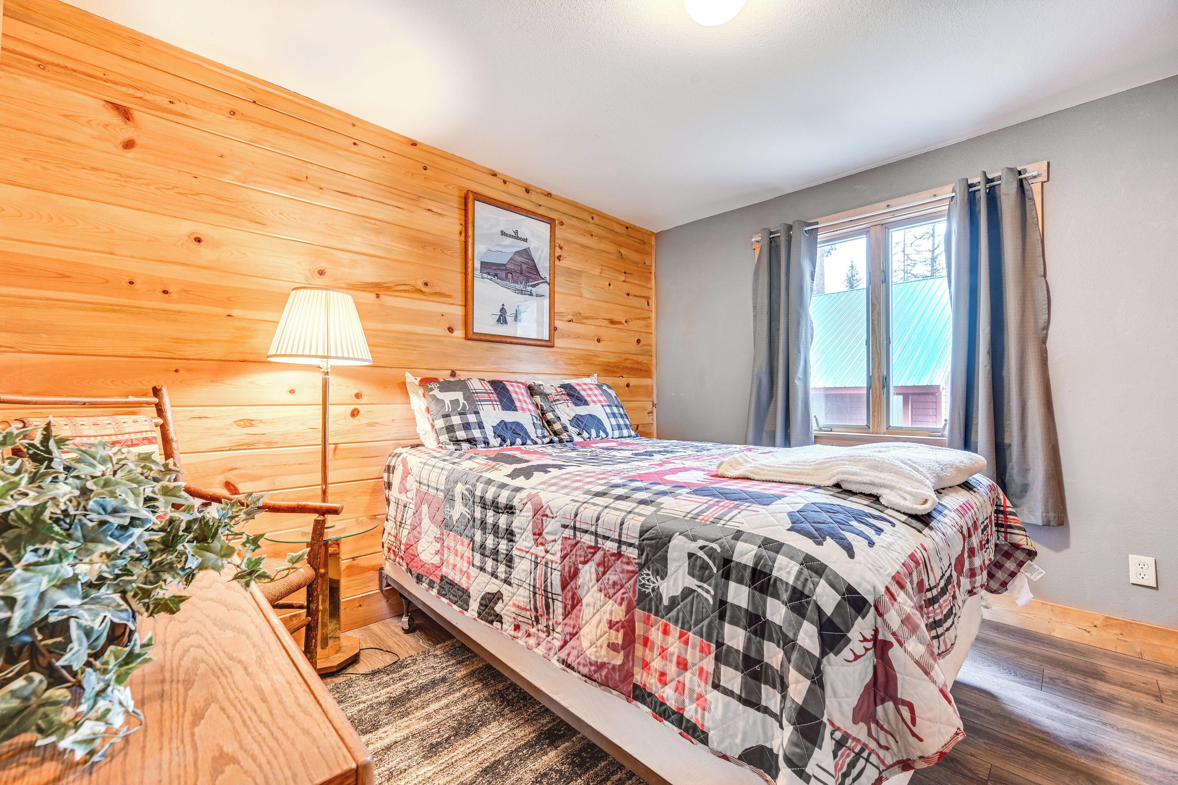 Een slaapkamer met een houten wand, een bed met een sprei, een lamp en een raam met gordijnen.