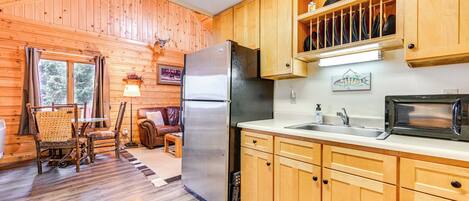 A wooden cabin interior with a kitchen area featuring a refrigerator, microwave, and wooden cabinets.