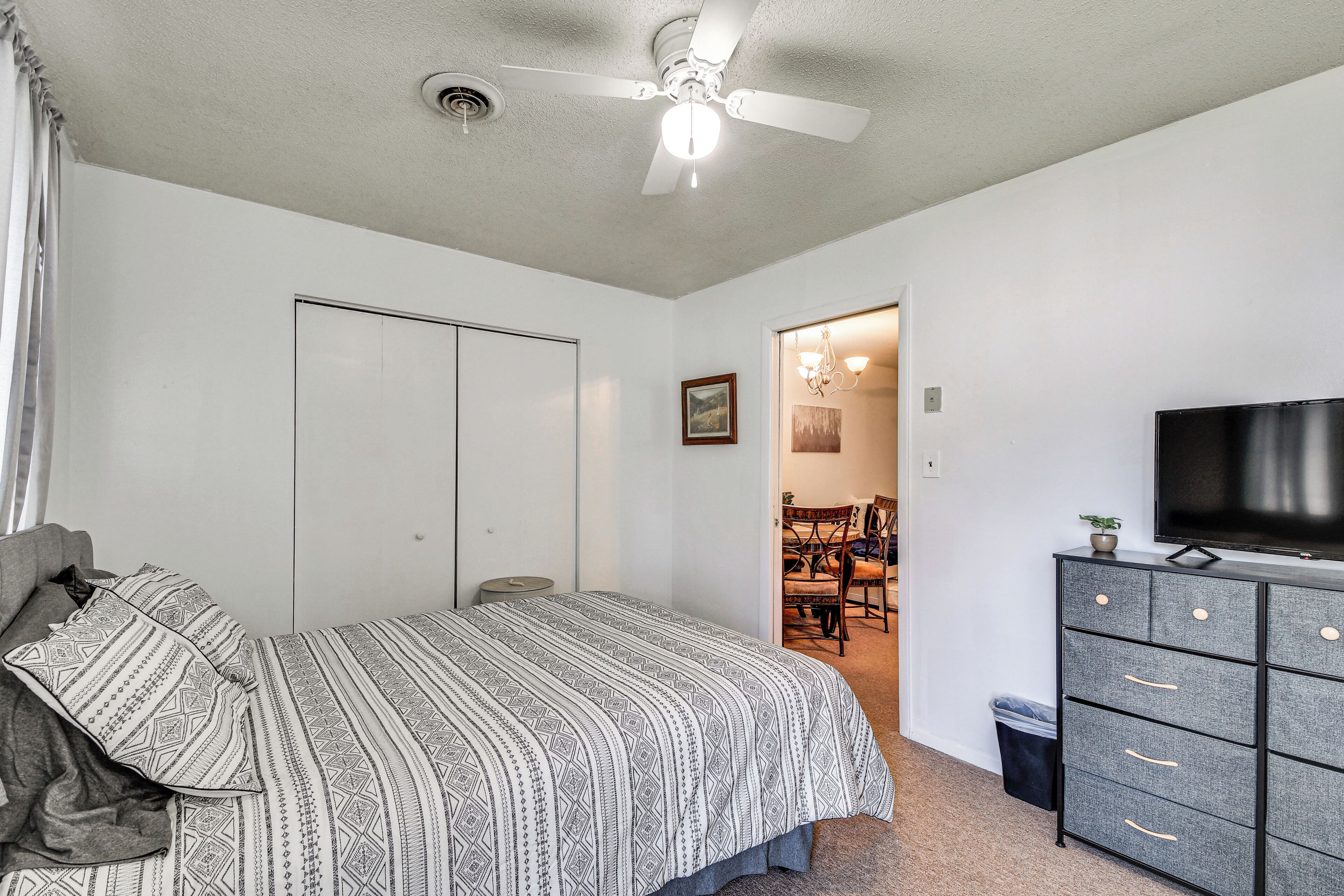 Une chambre à coucher avec un lit, une commode, un ventilateur de plafond et un téléviseur.