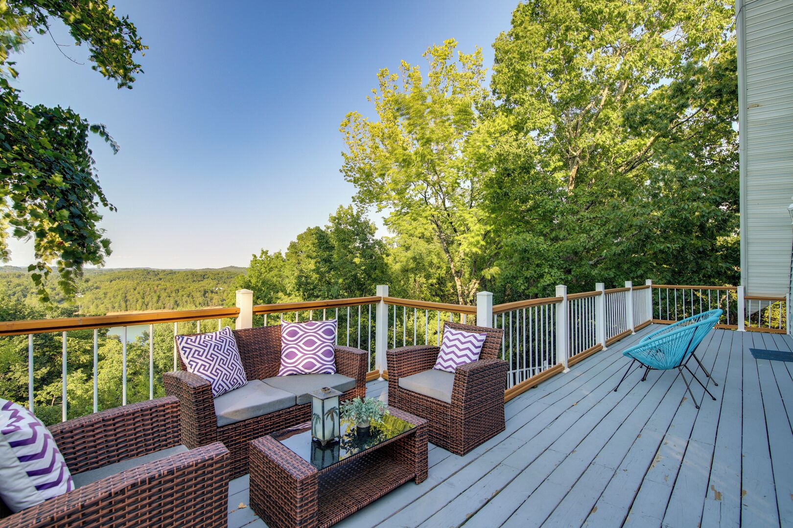 A deck with wicker furniture, a glass-top table, and a blue chair.