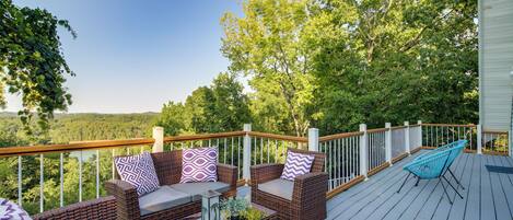 A deck with wicker furniture, a glass-top table, and a blue chair.