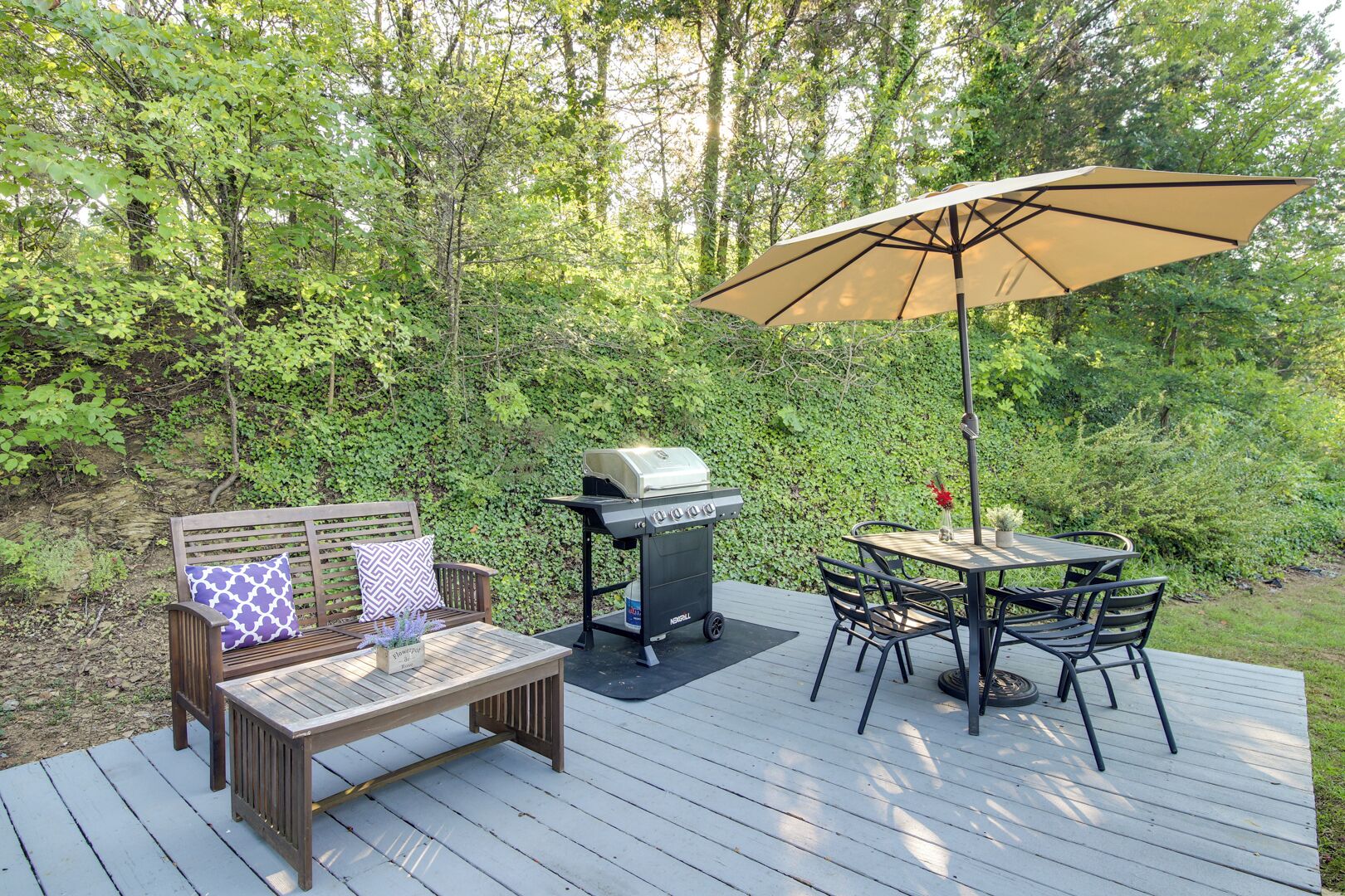 A deck with a grill, a table with chairs, and a bench with cushions.