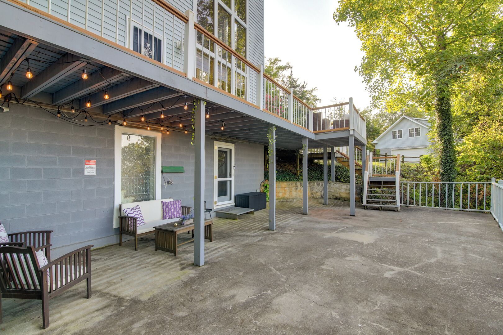 An outdoor patio area with a covered seating area, a wooden deck, and a view of a house in the background.