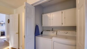 A laundry room with a washing machine and dryer, white cabinets, and a blue ironing board. - Smoky Mountains Cabin w/ Lake Access & Game Room! (Sevierville)