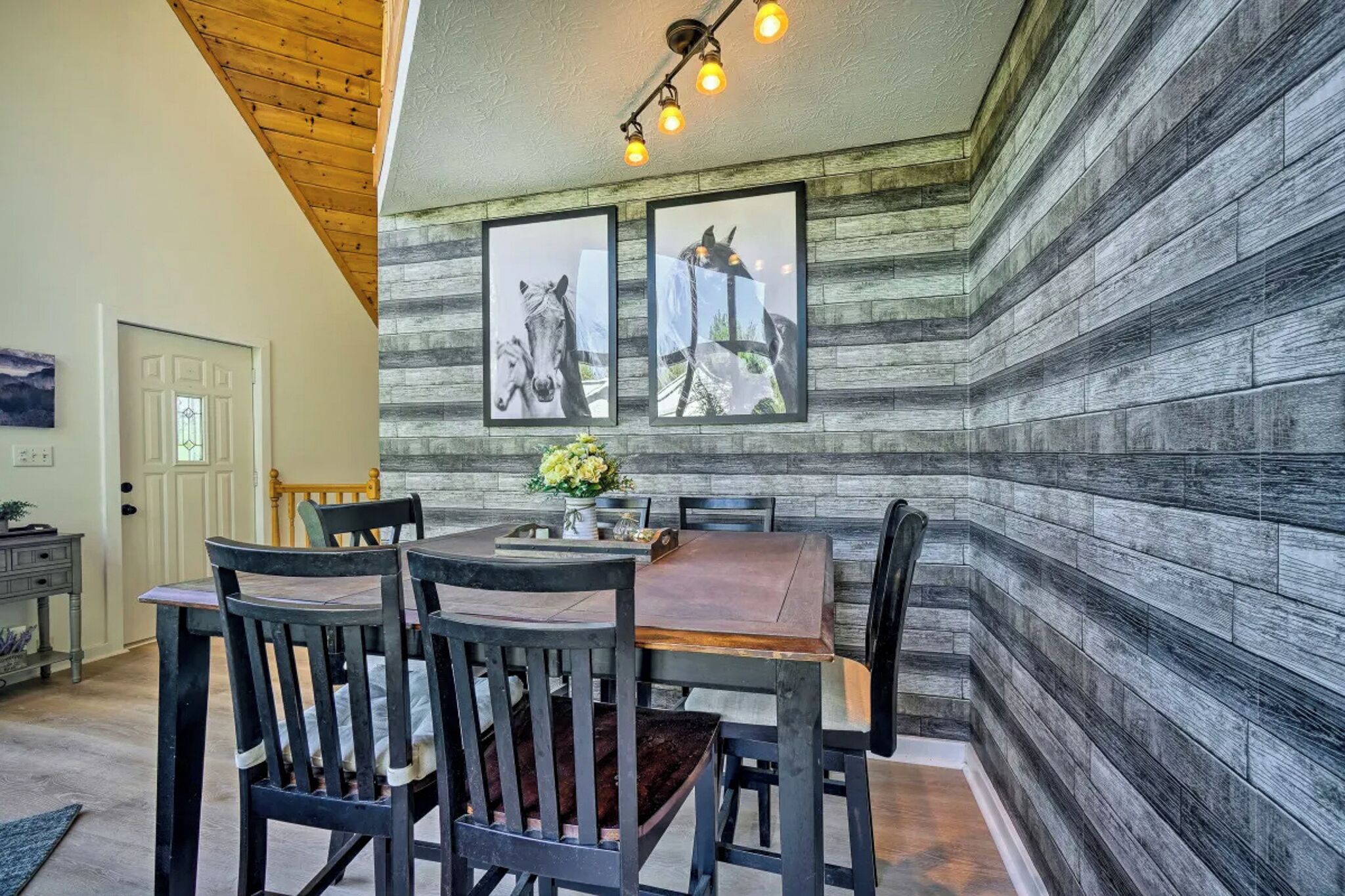 A dining area with a wooden table and chairs, framed horse pictures on the wall, and a ceiling light fixture.