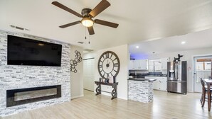 Un salon moderne avec une cheminée, une grande horloge murale et une cuisine en arrière-plan.