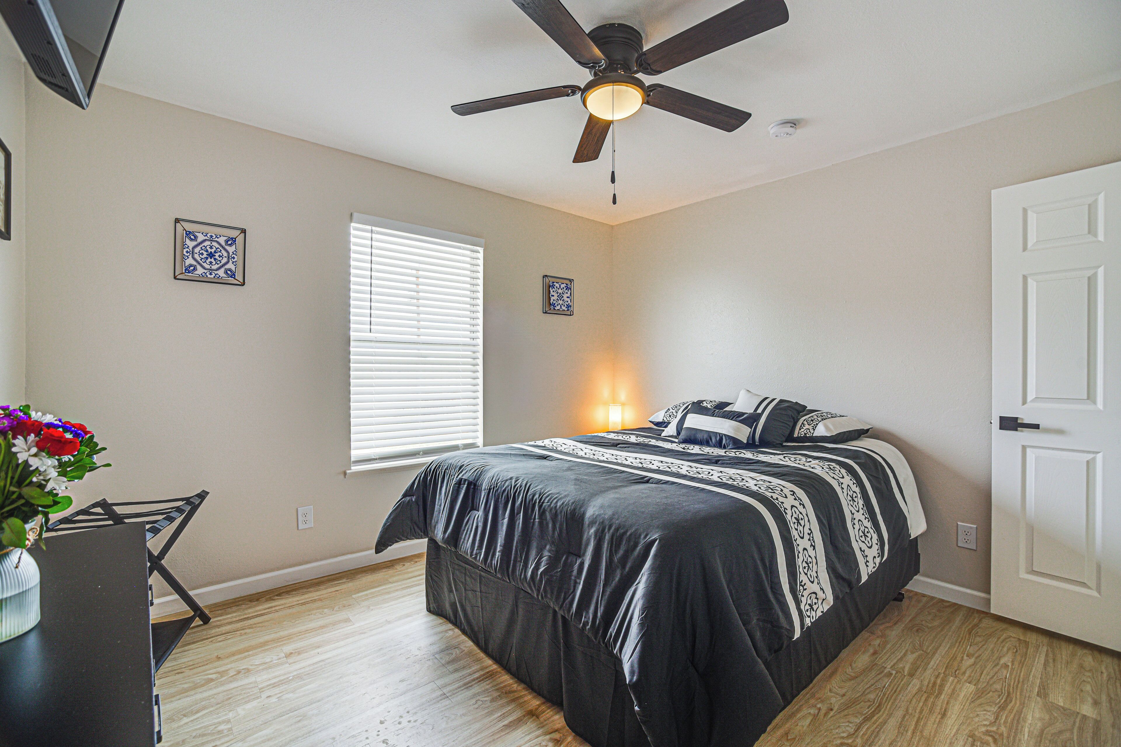 A bedroom with a bed, a ceiling fan, a window with blinds, and a door.