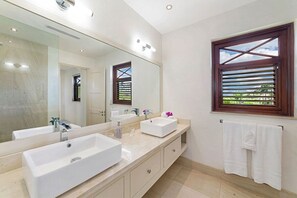 A modern bathroom with a large mirror, two sinks, a window with blinds, and a towel rack. - Infinity House by Blue Sky Luxury (Holetown)