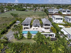 Une grande maison avec une piscine, entourée d’une végétation luxuriante et d’autres habitations.