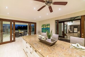 A modern kitchen with a large island, a ceiling fan, and a dining area with chairs and a table.