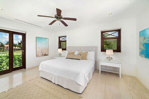 A bedroom with a bed, a ceiling fan, a nightstand, a lamp, and a window with a view.