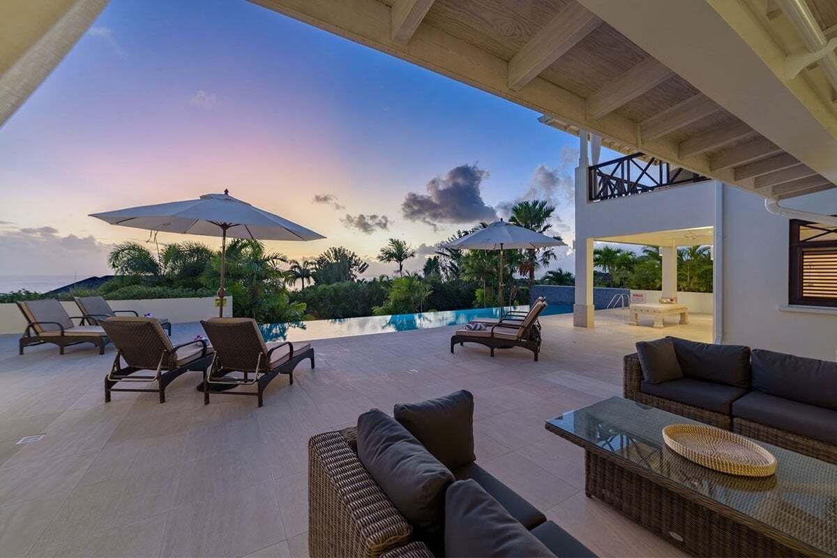 A rooftop lounge area with lounge chairs, a sofa, and umbrellas overlooking a swimming pool.