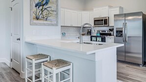 A modern kitchen with white cabinetry, stainless steel appliances, and a large island with bar stools. - Pelican Reef Or104 3 Bedroom Home by RedAwning (Rockport)