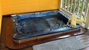 A hot tub on a wooden deck with a yellow wall and a painting of flowers.