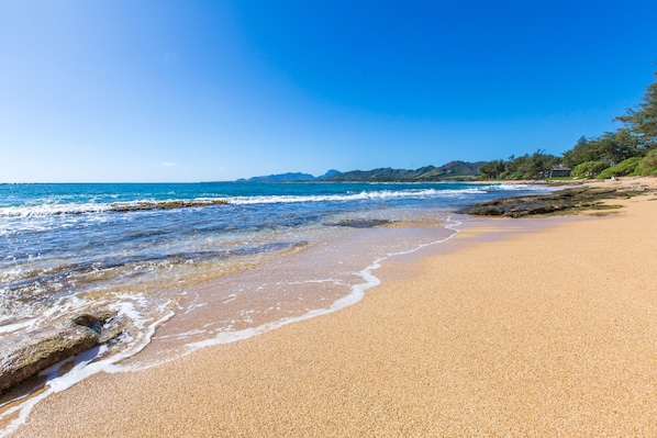 A beach with clear blue water, sandy shore, and distant mountains.