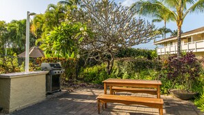 An outdoor patio with a wooden table and grill, surrounded by lush greenery and a palm tree. - Plantation Hale Suites F7, Ground Floor, AC, Walk to Beach (Kapaa)