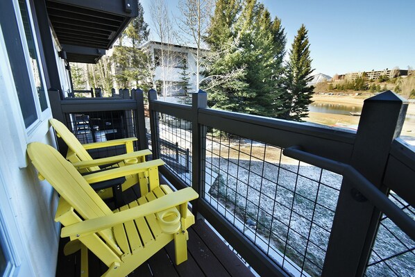 A balcony with yellow Adirondack chairs, a metal railing, and a view of a lake and trees.