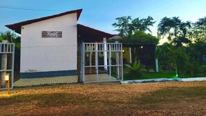 A small, single-story building with a white exterior and a red roof. It features a gated entrance with a metal fence and a small porch area. - Pousada Águas da Chapada (Carolina)