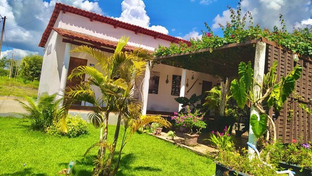 A house with a red-tiled roof, a white exterior, and a covered porch with plants. - Pousada Águas da Chapada (Carolina)