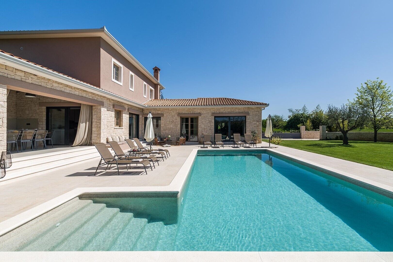 A modern house with a swimming pool, stone facade, and outdoor seating area.