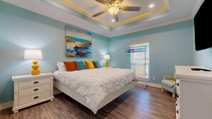 A bedroom with a bed, nightstands, a ceiling fan, a painting, a window with blinds, and a TV. - Salty Sea House: 3  BR, 2  BA House in Crystal Beach , Sleeps 12 (Bolivar Peninsula)