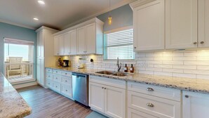 A kitchen with white cabinets, a dishwasher, a sink, and a window with blinds. - Salty Sea House: 3  BR, 2  BA House in Crystal Beach , Sleeps 12 (Bolivar Peninsula)