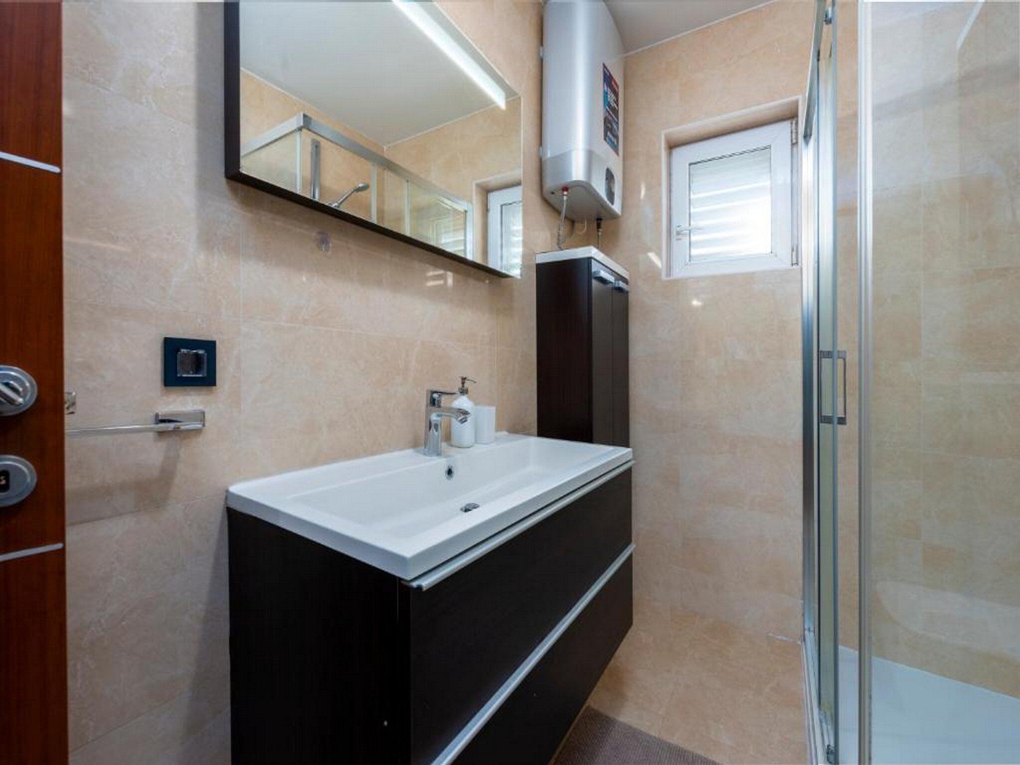 A modern bathroom with a white sink, dark cabinetry, a glass shower enclosure, and a mirror above the sink.