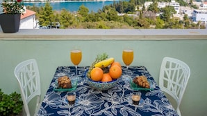 A table with a floral tablecloth, two white chairs, a bowl of fruit, two glasses of orange juice, and two small plates with pastries. - Apartments Meri & Karla (Dubrovnik)