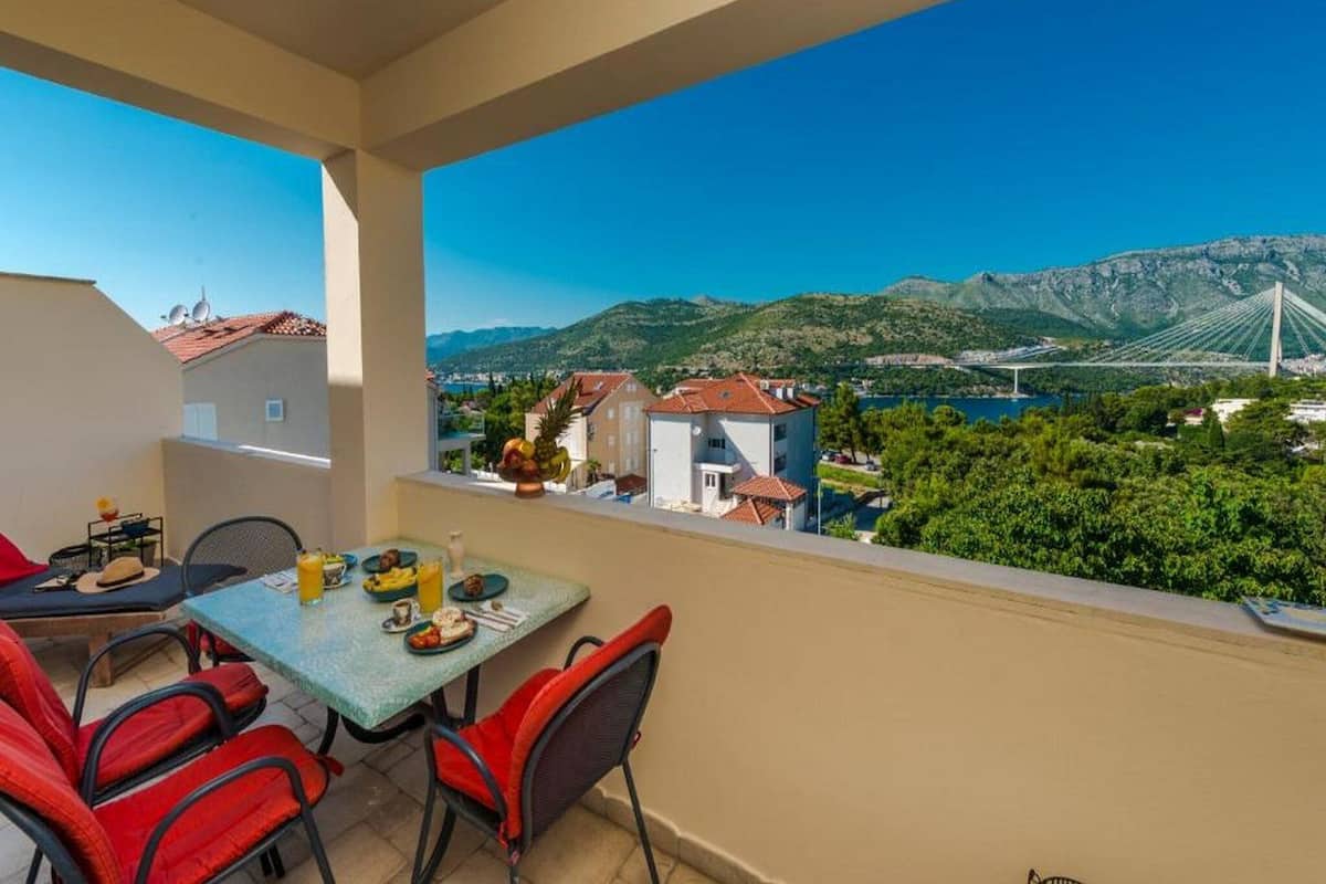 Ein Balkon mit Frühstückstisch, mit Blick auf eine Berglandschaft und eine Brücke.