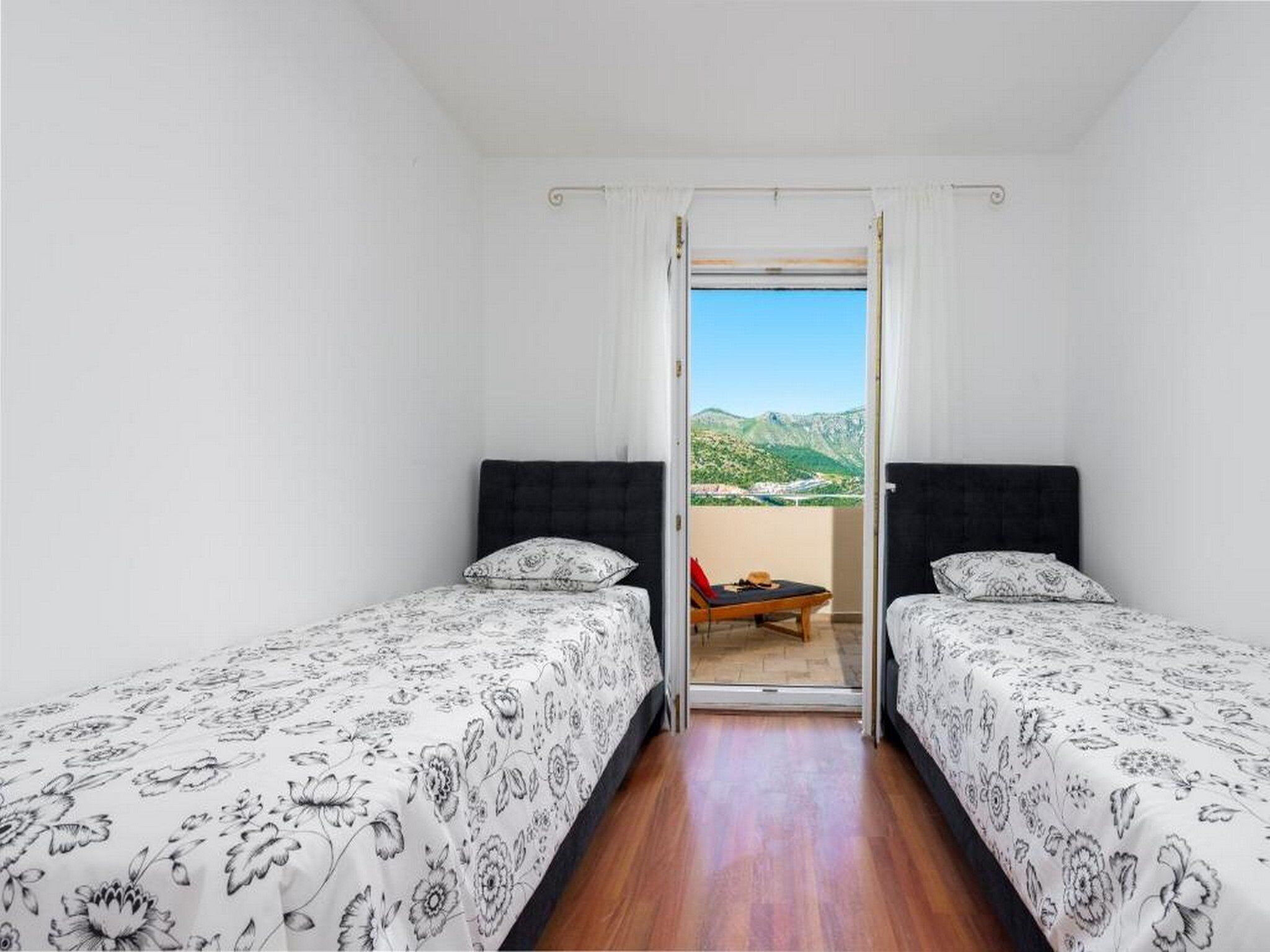 Een kamer met twee bedden, een kleintje tafeltje en uitzicht op een bergachtig landschap door een open deur.