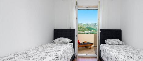Een kamer met twee bedden, een kleintje tafeltje en uitzicht op een bergachtig landschap door een open deur.