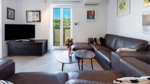 A modern living room with a flat-screen TV, leather sofas, a coffee table, and artwork on the walls. - Apartments Meri & Karla (Dubrovnik)