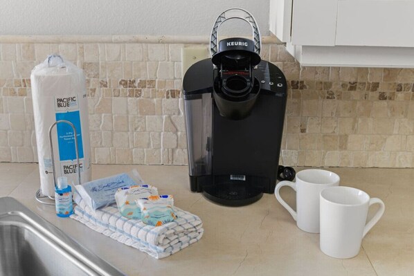 A kitchen with a Keurig coffee maker, a Pacific Blue 3-Ply Toweler, a bottle of water, and two white mugs on the counter.