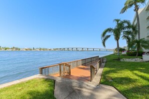 A waterfront walkway with a bridge in the background, a grassy area with palm trees, and a building with balconies. - Club Bahia Isla Del Sol 4th Floor! (Isla Del Sol)