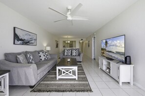 A modern living room with a grey sofa, a coffee table, a flat-screen TV, and a ceiling fan.